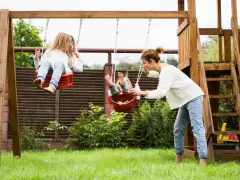 Mama pcha dzieci na huśtawkach, radosne zabawy dla dzieci na dworze.