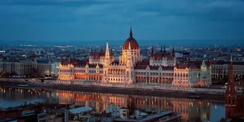 Budynek Parlamentu w Budapeszcie nocą, odbijający się w Dunaju. Miasto tętni życiem, aspirując do miana najbardziej imprezowych miast w Europie.