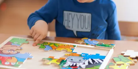 Chłopiec układa kolorowe puzzle ze zwierzątkami. Ukladanie puzzli co ćwiczy? Rozwija spostrzegawczość i zdolności manualne.