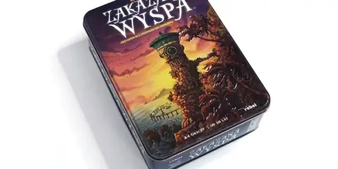 Pudełko gry planszowej "Zakazana Wyspa" z wieżą zegarową i palmami na tle zachodzącego słońca.