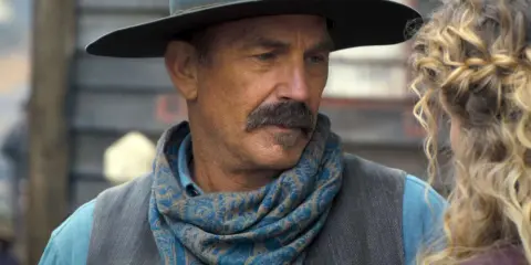 Kevin Costner w filmie z westernowym kapeluszem i chustą na szyi, rozmawia z kobietą.