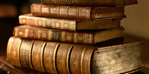 Stos starych, oprawionych w skórę ksiąg, z bogatymi zdobieniami grzbietów. Idealne do opowiadania historii, jak te, które znajdziemy w dobrej powieści historycznej.