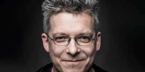Uśmiechnięty mężczyzna w okularach, z siwymi, nastroszonymi włosami. Może to być jeden z bohaterów Felix Net i Nika, gotowy na przygodę.