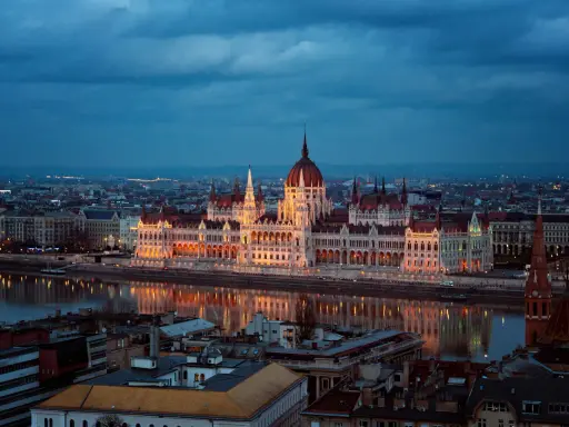 Budynek Parlamentu w Budapeszcie nocą, odbijający się w Dunaju. Miasto tętni życiem, aspirując do miana najbardziej imprezowych miast w Europie.