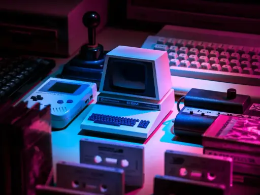 Retro gaming setup: Commodore CBM, Game Boy, joystick, keyboards, cassettes. Twój **słownik do gier** z lat 80. i 90.