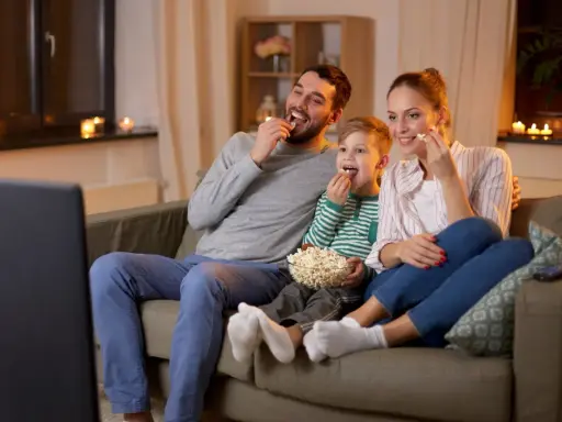 Rodzina śmieje się, jedząc popcorn podczas oglądania wzruszających filmów familijnych.