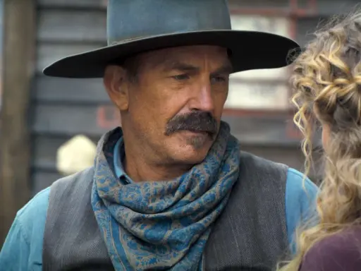 Kevin Costner w filmie z westernowym kapeluszem i chustą na szyi, rozmawia z kobietą.
