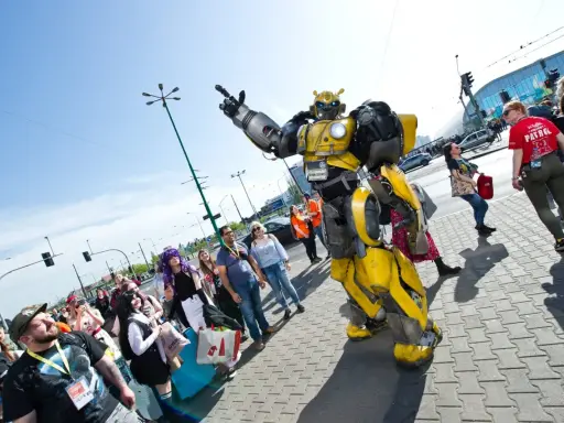 Bumblebee wita fanów na Pyrkonie. Tłum ludzi w kostiumach i z torbami idzie chodnikiem.