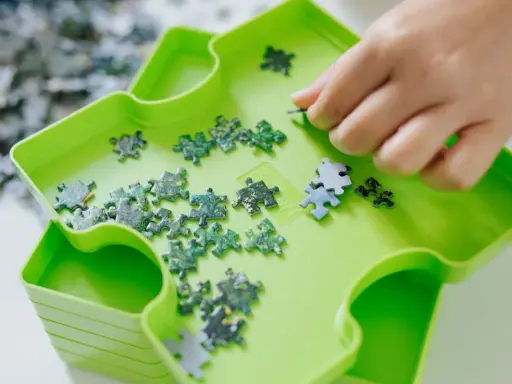 Dłoń układa zielone i niebieskie elementy układanki. To świetna zabawa, by układać puzzle po angielsku.