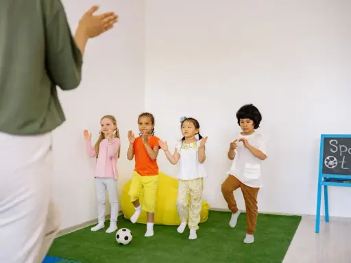 Dzieci ćwiczą przy tablicy z napisem "Sport time". Krótkie hasła sportowe dla dzieci motywują do ruchu.