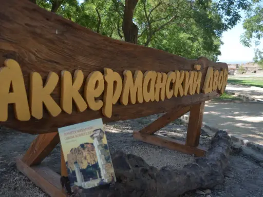 Drewniany napis "Аккерманский Двор" i książka "Sonety Krymskie" na tle stepów akermanskich i ruin.