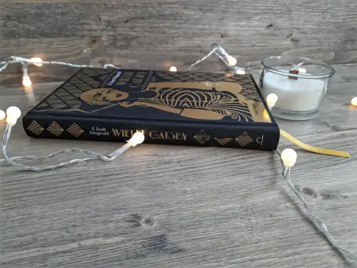 Książka "Wielki Gatsby" F. Scotta Fitzgeralda, otoczona świątecznymi lampkami, zaprasza do odkrycia jej streszczenia i historii.