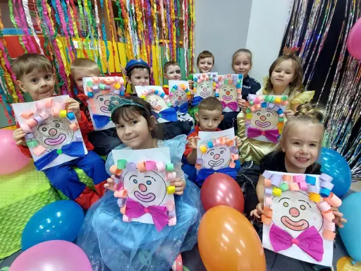 Dzieci w przedszkolu cieszą się z zabaw na balu karnawałowym, prezentując własnoręcznie wykonane prace z wizerunkami klaunów.