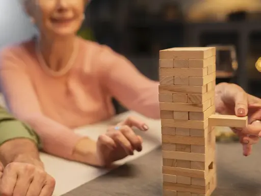 Uśmiechnięta seniorka wyciąga klocek z wieży Jenga. Wspaniałe konkursy zabawy dla seniorów!