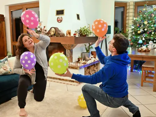 Para i dzieci bawią się balonami, wykonując twórcze zabawy ruchowe przy choince.