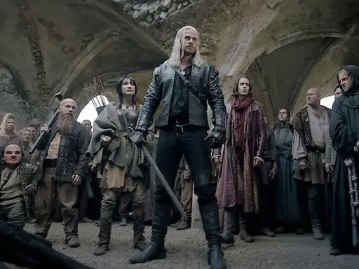 Geralt z Rivii stoi pośród tłumu, gdy ścieżki przeznaczenia w Wiedźminie splatają się. Widać krasnoludy, ludzi i zakapturzonych mnichów.