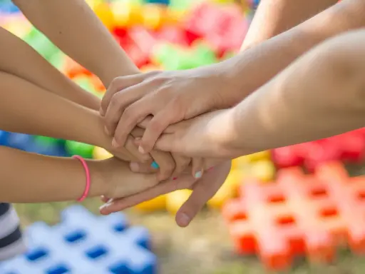 Dzieci łączą dłonie, symbolizując wspólne zabawy integracyjne. W tle kolorowe klocki.