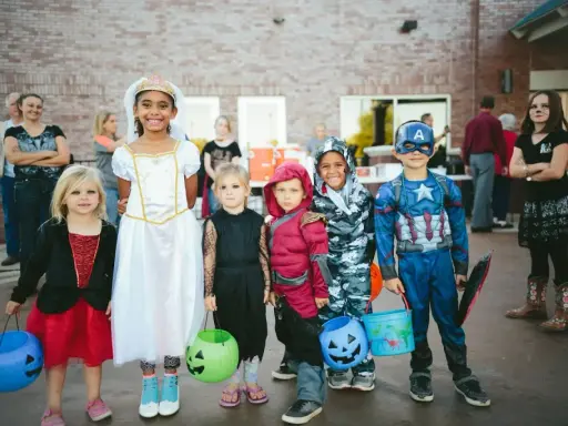 Dzieci w strojach na Halloween, gotowe na psikusy i zbieranie słodyczy. Wśród nich księżniczka, Kapitan Ameryka i inne postacie.