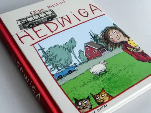 Okładka książki "Hedwiga" Fridy Nilsson, idealna dla 7 latka. Zabawna ilustracja z dziewczynką, owcą, kotami i autobusem.