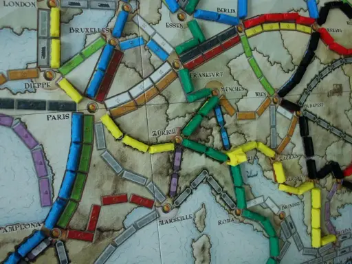 Planszowa mapa Europy z kolorowymi wagonikami. Która trasa jest najlepsza, by wsiąść do pociągu i odkryć nowe miasta?