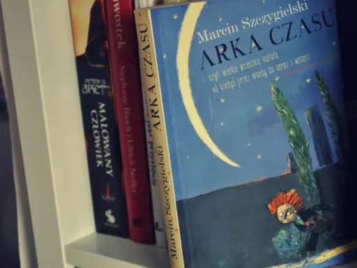 Książka "Arka Czasu" Marcina Szczygielskiego na półce. Ilustracja przedstawia nocne niebo z księżycem i biegnącą postacią.