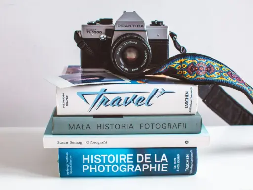 Stos książek o fotografii, w tym "Mała historia fotografii" i "Histoire de la photographie", z aparatem Praktica na górze.