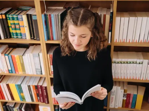 Dziewczynka z warkoczykami czyta książkę na tle regałów pełnych literatury. Może to być streszczenie "Skarbczyka" lub innej lektury.