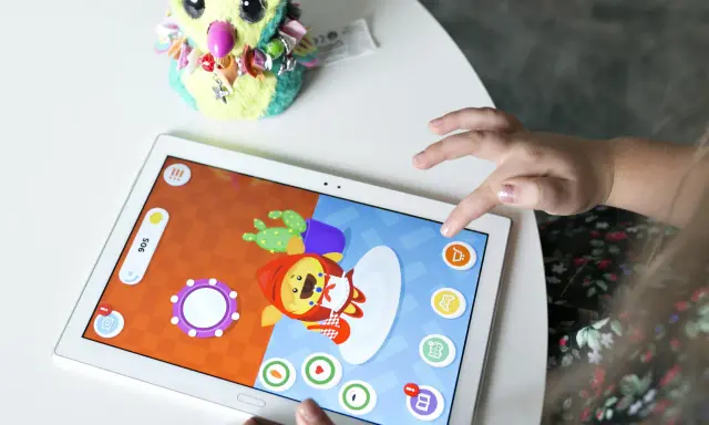 Dziecko gra w gry dla dzieci na telefonie, dotykając ekranu tabletu. Obok leży pluszowa sowa.