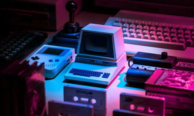 Retro gaming setup: Commodore CBM, Game Boy, joystick, keyboards, cassettes. Twój **słownik do gier** z lat 80. i 90.