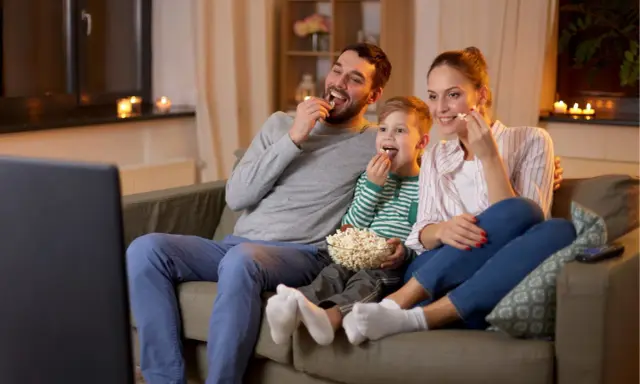 Rodzina śmieje się, jedząc popcorn podczas oglądania wzruszających filmów familijnych.
