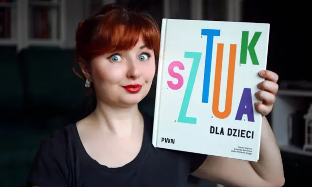 Kobieta z rudymi włosami trzyma książkę "Sztuka dla dzieci". Jej oczy są szeroko otwarte, a usta umalowane na czerwono.