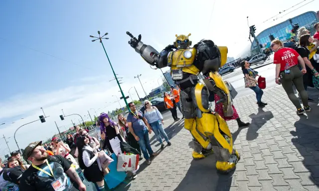 Bumblebee wita fanów na Pyrkonie. Tłum ludzi w kostiumach i z torbami idzie chodnikiem.