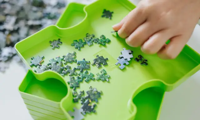 Dłoń układa zielone i niebieskie elementy układanki. To świetna zabawa, by układać puzzle po angielsku.