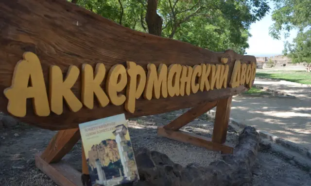 Drewniany napis "Аккерманский Двор" i książka "Sonety Krymskie" na tle stepów akermanskich i ruin.