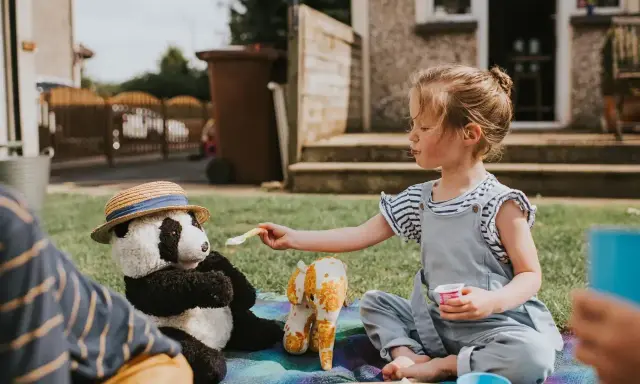 Dziewczynka karmi pluszową pandę na pikniku. Świetny sposób, co robić na nudę w ogrodzie!