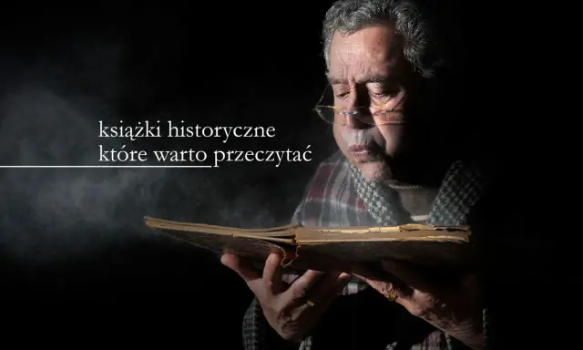 Starszy mężczyzna w okularach pochyla się nad starą księgą, zanurzając się w lekturze. Wokół unosi się pył, podkreślając atmosferę tajemnicy i wiedzy zawartej w książkach historycznych.