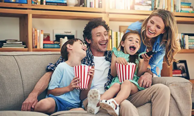 Rodzina śmieje się do rozpuku, jedząc popcorn podczas oglądania filmu dla całej rodziny.