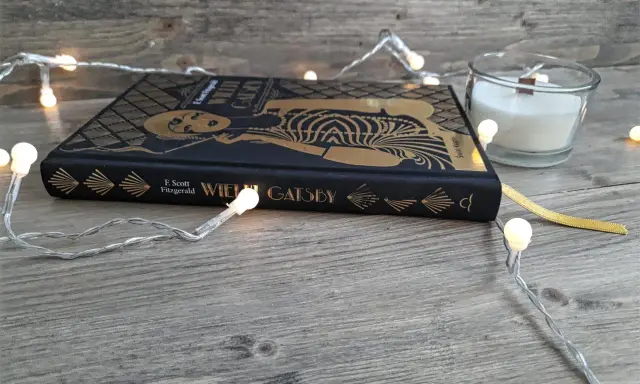Książka "Wielki Gatsby" F. Scotta Fitzgeralda, otoczona świątecznymi lampkami, zaprasza do odkrycia jej streszczenia i historii.