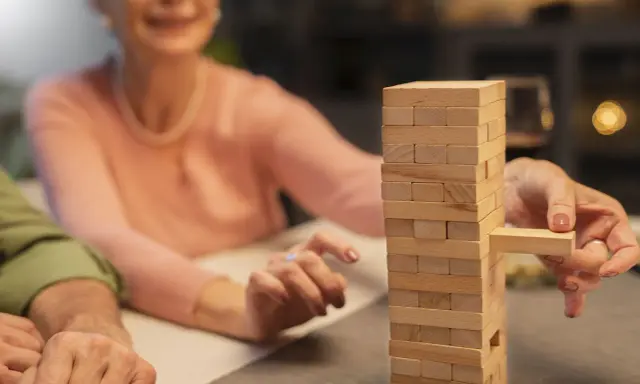 Uśmiechnięta seniorka wyciąga klocek z wieży Jenga. Wspaniałe konkursy zabawy dla seniorów!