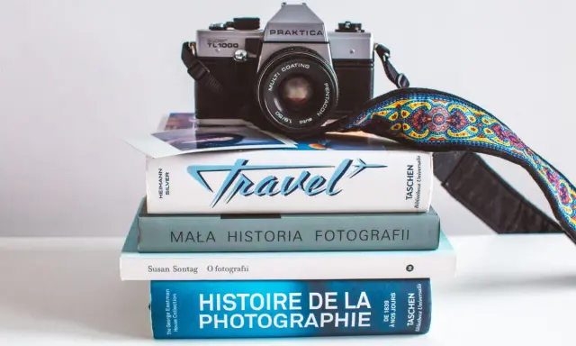 Stos książek o fotografii, w tym "Mała historia fotografii" i "Histoire de la photographie", z aparatem Praktica na górze.