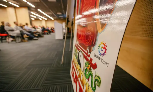Na konferencji o grach planszowych, z bliska widać planszę z logo "gamedesire" i smoczym motywem.