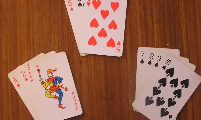 Karty na drewnianym stole: as, dwójka, joker i inne. Joker w kartach wygląda jak wesoły błazen.