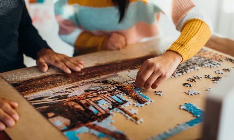 Dwie osoby składają puzzle, tworząc obraz. To dowód na to, że najlepsi producenci puzzli tworzą dzieła, które łączą ludzi.