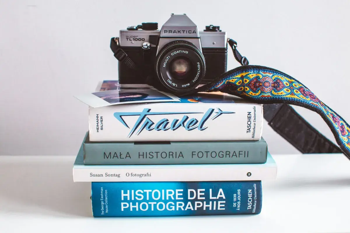 Stos książek o fotografii, w tym "Mała historia fotografii" i "Histoire de la photographie", z aparatem Praktica na górze.