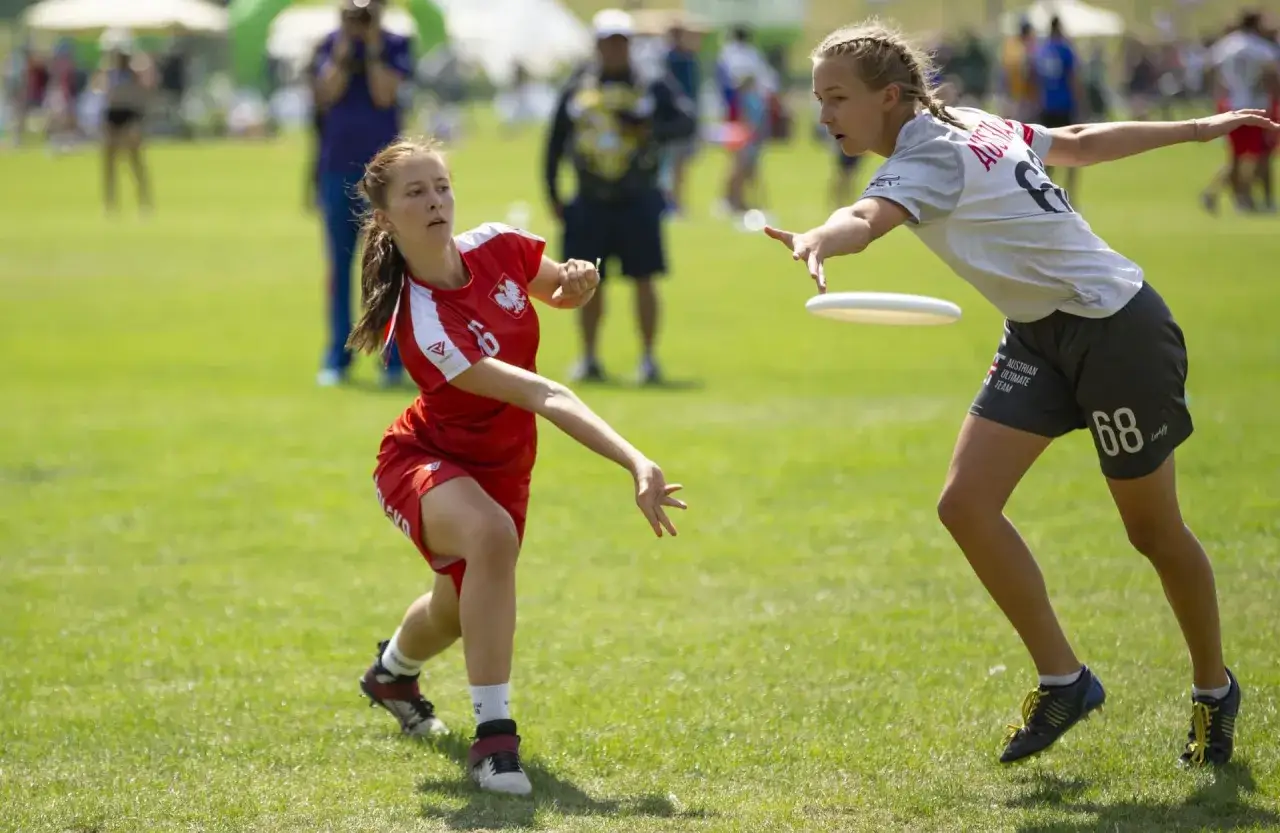 Dwie dziewczyny grają w ultimate frisbee, to świetne gry plenerowe dla młodzieży. Jedna rzuca dyskiem, druga pr&oacute;buje go złapać.