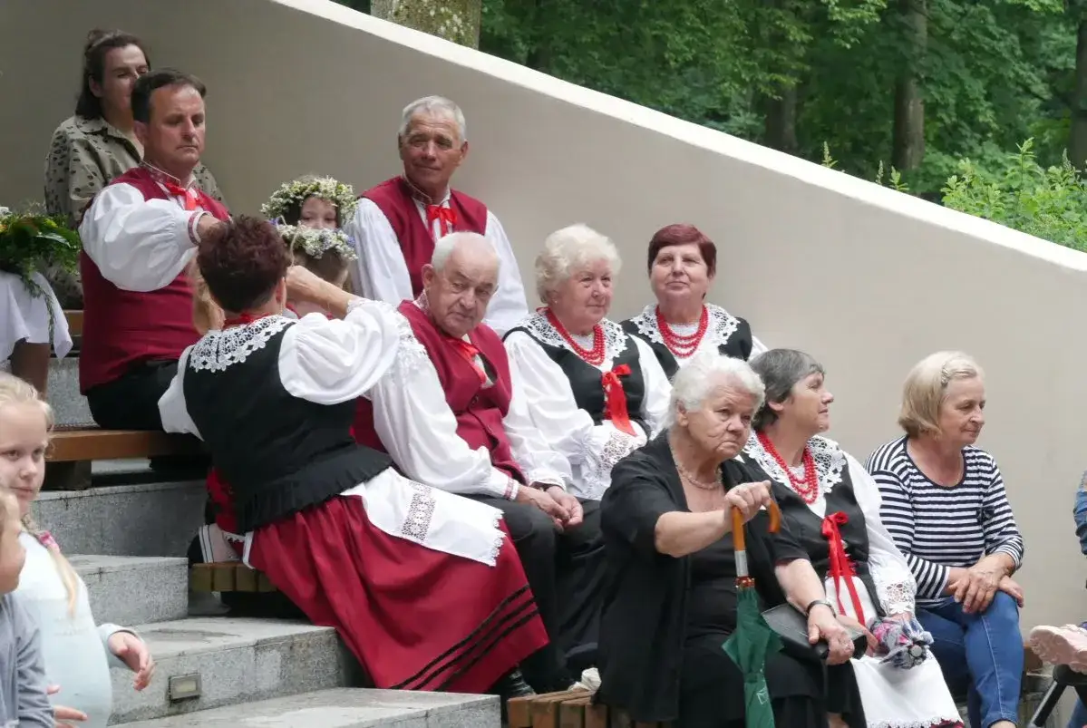 Ludzie w strojach ludowych, przygotowujący się do pieśni świętojańskiej o sob&oacute;tce. Wianek na głowie dziewczynki.