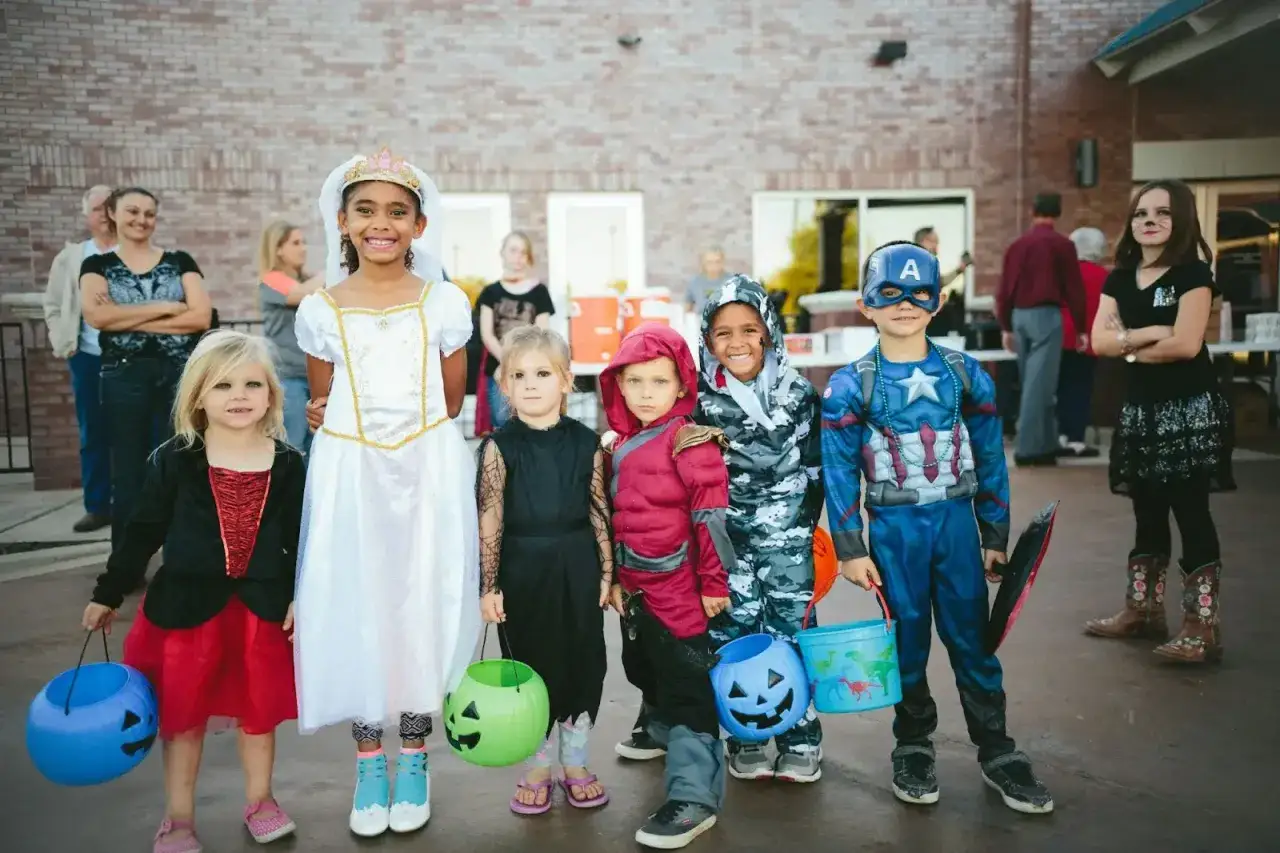 Dzieci w strojach na Halloween, gotowe na psikusy i zbieranie słodyczy. Wśród nich księżniczka, Kapitan Ameryka i inne postacie.