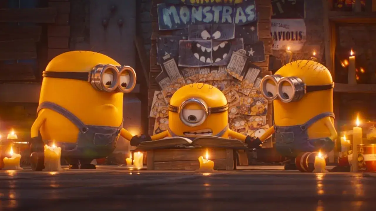Trzech minionków otacza świece, jeden czyta książkę. W tle plakaty z potworami, jakby przygotowywali się do kolejnych części przygód.