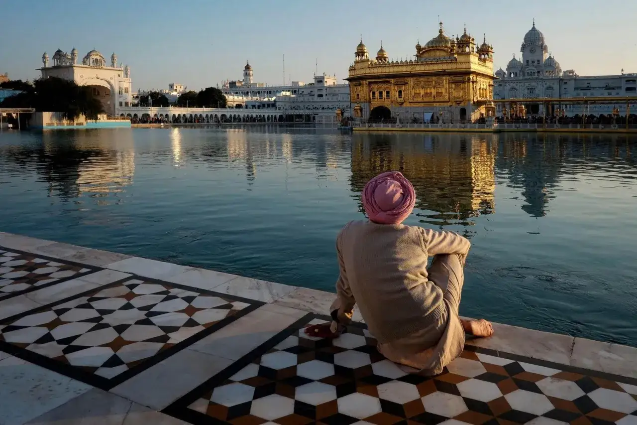Mężczyzna w różowym turbanie siedzi nad wodą, myśląc o Indiach. Złota Świątynia Harmandir Sahib w Amritsarze.
