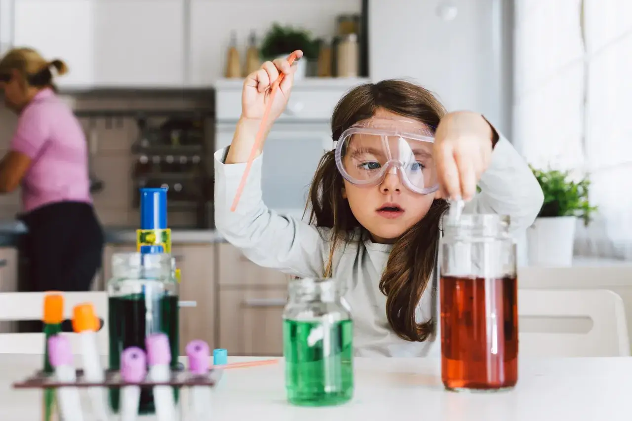 Mała chemik w okularach ochronnych miesza płyny w słoikach. Ciekawe zabawy dla dzieci w domu 10 lat.